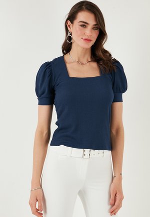 Navy blue textured top with a square neckline and puff sleeves, paired with white pants. Simple design, emphasizing shape and fit.