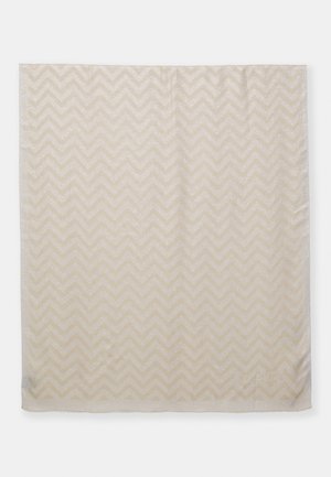 Beige stof met een subtiel chevronpatroon in een licht glanzende textuur, plat gelegd met zachte plooien en kreukjes zichtbaar.