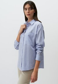 Blauw-witte gestreepte overhemd met knopen, een kraag, lange mouwen en een borstzak. Gemaakt van een lichte stof.