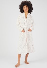Robe bianca con una texture morbida e pelosa e sottili macchie beige. Presenta un collo sciallato, una cintura e due tasche anteriori. Lunghezza a metà polpaccio.
