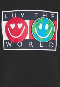 Maglietta nera con una grafica che mostra due facce sorridenti, una rossa con occhi a cuore e un pianeta blu. Il testo recita "AMA IL MONDO."