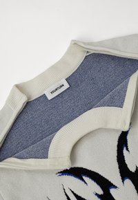 Πλεκτή μπλούζα με κολάρο σε κρέμα απόχρωση και υφή μπλε επένδυση. Το σώμα φέρει γραφικό σχέδιο σε μαύρο και μπλε χρώμα.