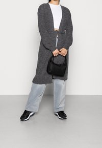 Lång cardigan med öppen front i mörkgrått stickat material, med en lös passform och ribbad textur. Tillsammans med ljusblå vida byxor och en svart handväska.