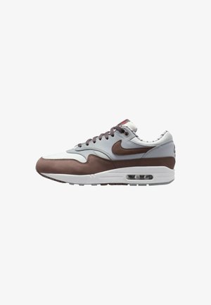 Sneaker Nike Air Max 1 avec un sommet en cuir gris clair et marron, un col rembourré et une unité d'air visible dans la semelle.