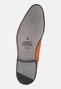 Schuhsohle aus grauem und orangefarbenem Leder, mit einer schwarzen Gummispitze und metallischen Akzenten, geprägtem Branding und runder Form.