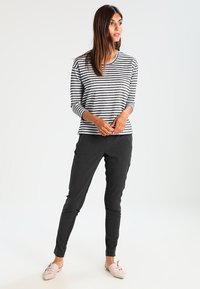 Camisola de mangas longas riscada em branco e cinza escuro, combinada com calças ajustadas pretas. Tecido macio com um design descontraído e decote redondo.