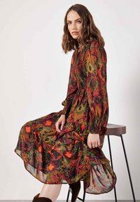 Langes, transparentes Kleid mit floralem Muster in Rot, Orange und Grün. Geraffter Mieder und lange Ärmel. Fließender Rock mit gewelltem Saum.