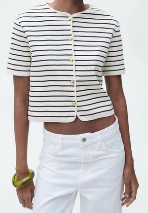 Person wearing a short-sleeve white crop top with black horizontal stripes and gold buttons, white pants, and a green bracelet on left wrist.