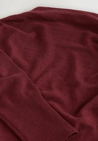 Burgundowa dzianinowa sweter o miękkiej teksturze, z klasycznym okrągłym dekoltem i prążkowanymi mankietami, ułożony w luźnej, pogniecionej pozycji.