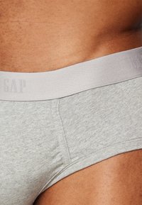 Grau Baumwollslip mit einem weichen Gummibund. Der Stoff hat eine glatte Textur mit einem dezenten Melange-Muster. Das Logo ist im Bund eingeprägt.