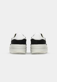 Svart och vit plattformssneakers med en slät läderövre och texturerade svarta mockadetaljer. Tjock vit gummisula.