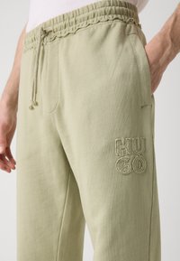 Hellgrüne Sweatpants mit einem elastischen Bund, seitlichen Taschen und einem strukturierten gestickten Logo "HUGO" auf dem linken Oberschenkel.