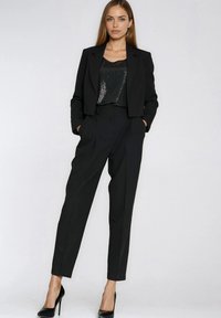 Czarna krótka marynarka na sequinowanym czarnym topie, zestawiona z czarnymi, wysokim stanem spodnie i szpilkami. Gładki i dopasowany fason.