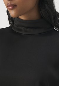 Top negro de cuello cisne corto con una textura lisa y brillante. Presenta un diseño ajustado y un sutil drapeado en el escote.