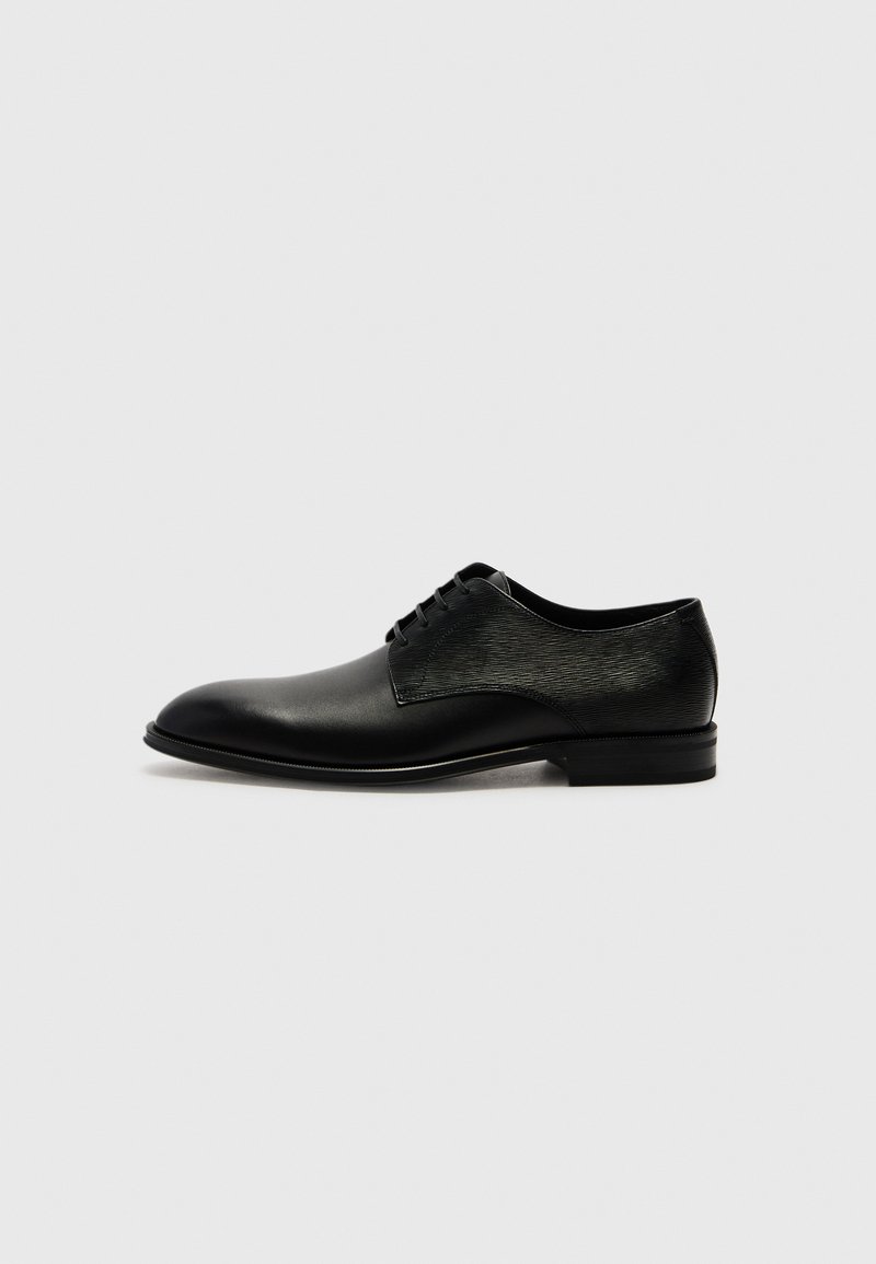 Svart lærsko med en glatt finish foran og en teksturert panel på siden, med rund tå og snøring.