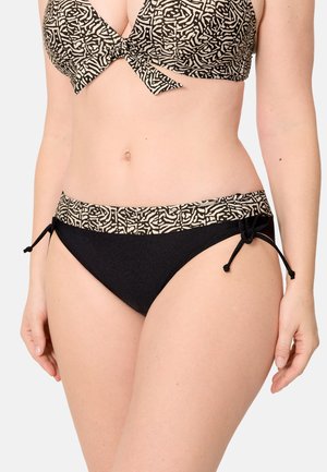 Mujer con braga de bikini negra con cinturilla estampada y lazos laterales, combinada con un top de bikini a juego estampado.