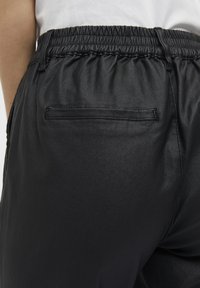 Sorte elastiske bukser med taljebånd lavet af et glat, skinnende materiale, med en enkelt baglomme og et afslappet fit design.