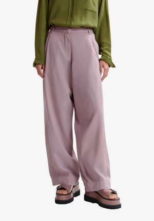 Pantaloni lilla a gamba larga indossati con camicia verde a maniche lunghe e sandali platform massicci viola con suole nere.