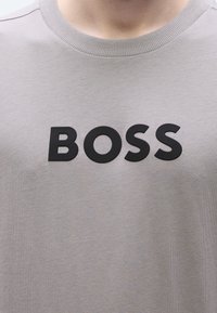 Γκρι μπλουζάκι με ριμπ λαιμόκοψη και μαύρο, έντονο λογότυπο "BOSS" στο στήθος. Απαλή υφή και απλός σχεδιασμός.
