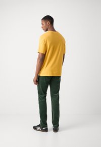 Kortermet gul bomull T-skjorte, grønne cordbukser og svarte sneakers med hvite striper. Fokus på rene linjer og avslappet passform.