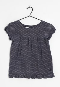 Tmavě modré tričko s krátkými rukávy a volánkovým lemem, zdobené geometrickým vzorem malých trojúhelníků v světlejších odstínech. Bavlněný materiál, volný střih.