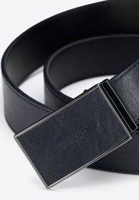 Skórzany pasek w ciemnym granacie z teksturowanym wykończeniem, z prostokątną metalową klamrą z wygrawerowanym logo i kontrastowym przeszyciem.