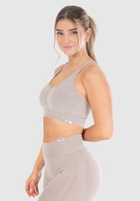  Sujetador deportivo gris claro con una textura suave, que presenta un detalle de costura central y tirantes finos, combinado con leggings de talle alto a juego.