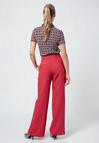 Red wide-leg pants with a high waist, paired with a short-sleeved blouse featuring a black and white spiral pattern. Textured fabric, sleek design.