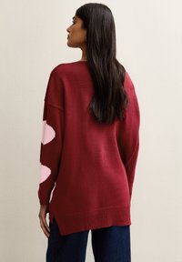 Burgundy knitted sweater with pink leaf-shaped patterns, crew neckline, and side slits. Textured, soft material; relaxed fit.