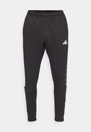Čierne športové nohavice s elastickým pásom, zdobené bielym logom Adidas a bočnými akcentmi. Hladká tkanina s zúženým strihom.