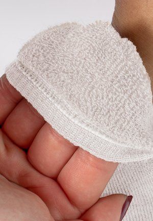 Ręka trzymająca biały, teksturowany materiał z elastycznym brzegiem, ukazująca szczegóły dzianiny i miękkie pętelki na jasnym tle.