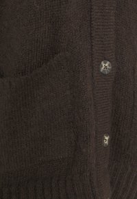 Hnědý strukturovaný pletený kardigan s knoflíkovým zapínáním a dv ěma předními kapsami. Obsahuje žebrovaný lem a hladké knoflíky.