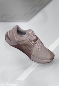 Lys mauve sportssko med mesh-overdel, kontrasterende mørk mauve sål, snørebåndsdesign og logo accenter på siden og tungen.