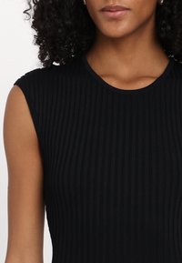 Top preto canelado sem mangas com um decote redondo e um tecido texturizado, apresentando riscas verticais visíveis e um acabamento suave.
