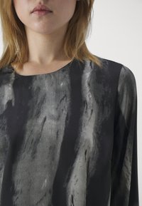 Bluză cu mânecă lungă din țesătură neagră și gri, având o textură netedă cu modele abstracte, decolteu rotund și croi lejer.