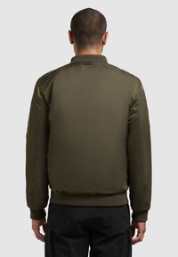 Olivegrüner Bomberjacke mit glatter, glänzender Textur. Mit gerippten Manschetten und Saum. Mit Reißverschluss gesichertem Fach am linken Ärmel.