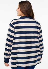 Pikem varrukaga triibuline särk, mis on kujundatud tumesiniste ja kreemjate horisontaalsete triipudega, krae ja lõdva sobivusega. Pehme kangas, millel on sile tekstuur.