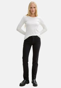 Maglietta bianca a maniche lunghe con scollatura tonda, abbinata a pantaloni neri aderenti e scarpe nere con suola chunky. Tessuto semplice e liscio.