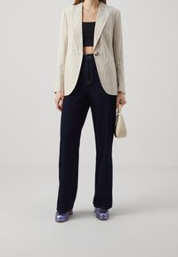 Beige striped blazer with a single button, paired with dark blue wide-leg jeans and shiny purple platform shoes. Small white handbag.