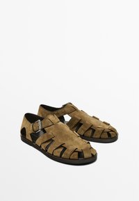 Sandali in suede marrone con un design aperto caratterizzato da cinturini intagliati, chiusura con fibbia regolabile e suola piatta nera.