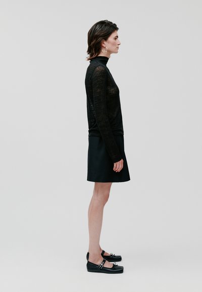 Haut noir transparent à manches longues, jupe noire et chaussures plates noires. Design simple avec peu de matériaux et sans motifs.