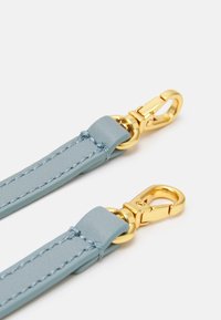 Correa de cuero azul claro con clips de metal dorado. Presenta una textura suave y costuras precisas, diseñada para sujetar objetos de forma segura.
