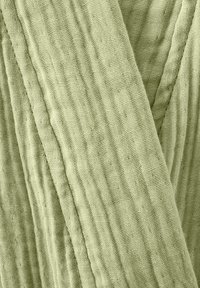 Tissu texturé vert clair avec un motif froissé, mettant en valeur un design tissé. Le matériau semble doux et respirant.