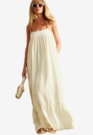 Robe maxi couleur crème avec un buste ajusté et un ourlet évasé. Présente des fines bretelles avec des accents en perles. Texture douce et fluide.