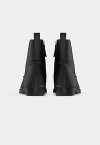 Pár čiernych kožených ankle boots zobrazených zozadu, s ťahacími pútkami a bočnými zipsami na bielom pozadí.