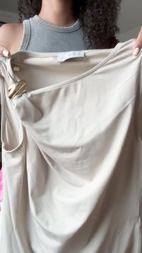 Bež ükste ilma varrukateta tipp, millel on volditud disain, millel on dekoratiivne kuldne riistvara aktsent õlal, valmistatud siledast kangast.