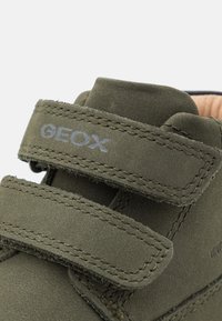 Zelené semišové boty s dvěma suchými zipy, s šedým logem GEOX. Měkká vnitřní podšívka a zesílené švy na okrajích.