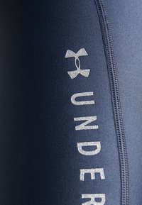 Laivastonsiniset urheilutrikoot, joissa on sileä pinta ja metallinhohtoinen hopeinen logo sekä merkin nimi sivusaumassa.