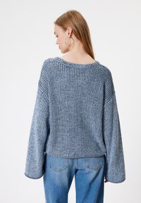 Sweter dzianinowy w jasnoniebieskim kolorze o luźnym, oversize'owym kroju, z szerokimi rękawami i prążkowaną fakturą. Para jasnoniebieskich dżinsów dopełnia cały wygląd.