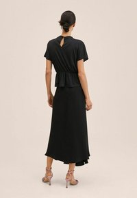 Top negro de peplum con mangas cortas y detalle de ojal en la espalda, combinado con una falda maxi negra fluida y tacones altos rosas con tiras.